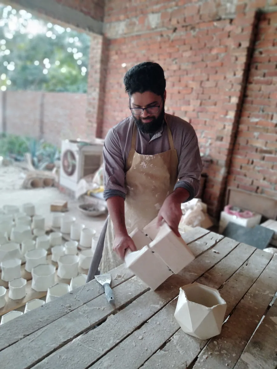 Lifting a two-part plaster mould beside rows of freshly cast pieces left to dry